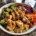 Close-up of a Protein Packed Thai Peanut Chicken Bowl featuring grilled chicken, broccoli, shredded carrots, red cabbage, and quinoa drizzled with peanut sauce.