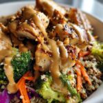 Close-up of a Protein Packed Thai Peanut Chicken Buddha Bowl with grilled chicken, broccoli, carrots, and peanut sauce over quinoa.