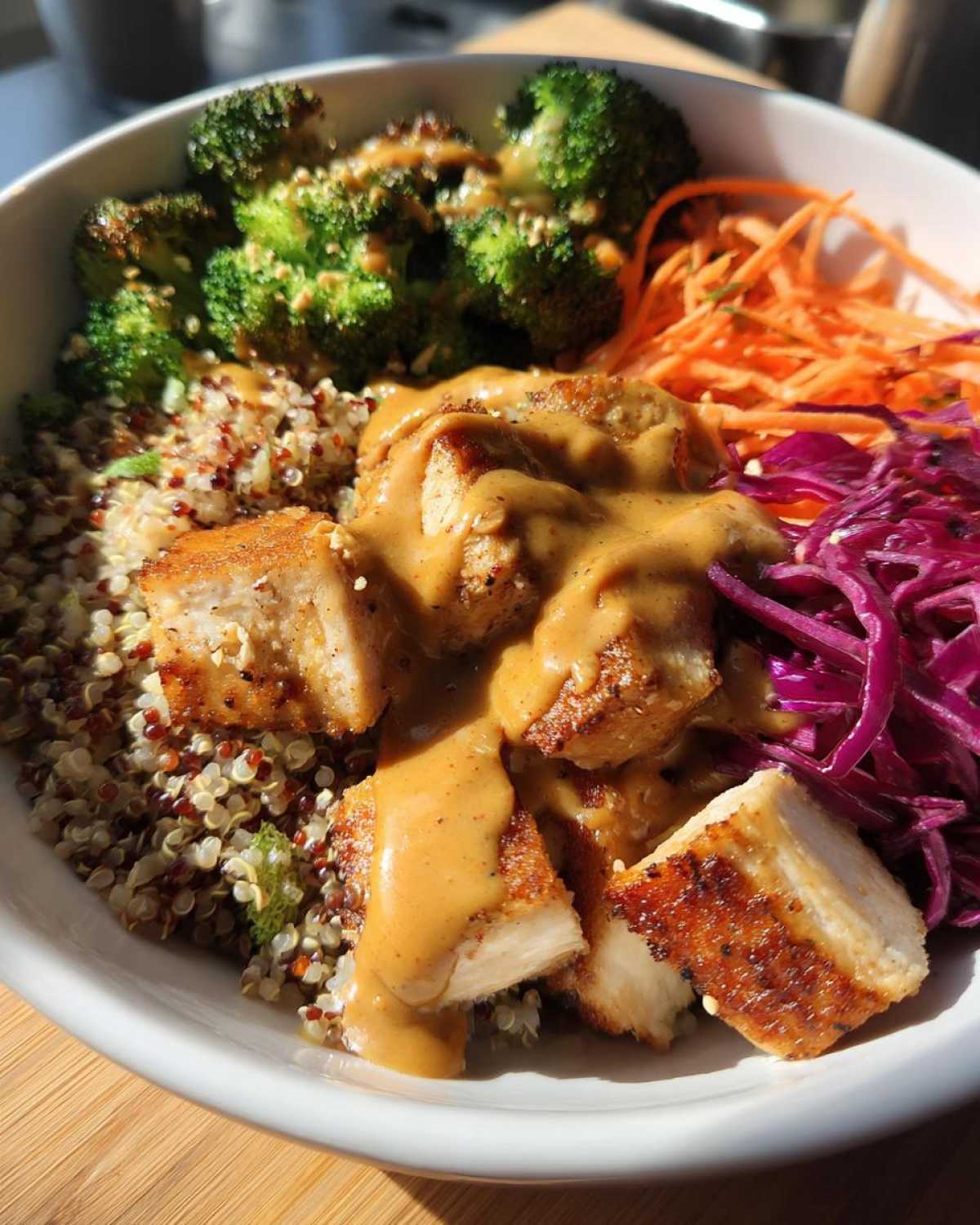 Close-up of a Protein Packed Thai Peanut Chicken Bowl with quinoa, broccoli, carrots, and peanut sauce.