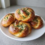 Four golden brown Quick Sourdough Discard Garlic Knots topped with minced garlic and fresh parsley on a white plate.