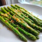 A close-up of bright green Roasted Asparagus with Garlic and Lemon, served on a white plate.