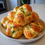 A close-up of a mound of soft, golden-brown Garlic Knots drizzled with butter and sprinkled with fresh parsley.
