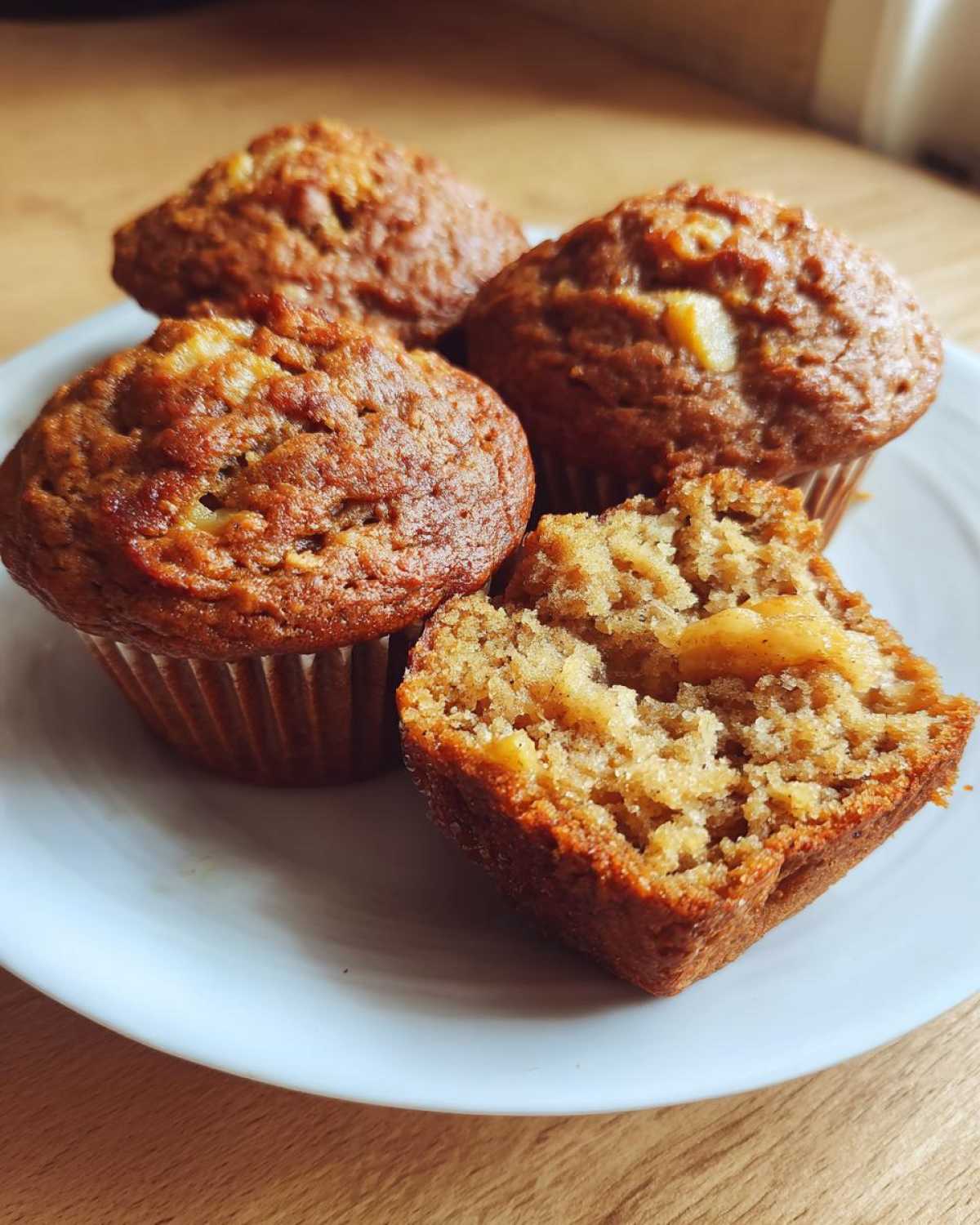 Three whole and one halved Sourdough Discard Apple Muffins showing the moist interior texture on a white plate.