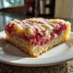 A close-up of a square slice of Strawberry Shortcake Bars with bright red fruit filling and white glaze drizzle.