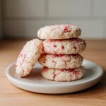 A stack of four delicious Strawberry Shortcake Butter Cookies with pink strawberry pieces visible, resting on a speckled white plate.