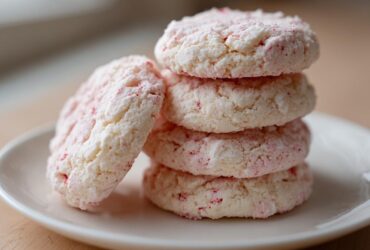 A stack of four soft, white Strawberry Shortcake Butter Cookies with pink flecks on a white plate.