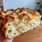 A close-up, cross-section view of a thick slice of Tasty Garlic Bread With Cheese, showing the airy interior and melted, browned cheese topping.