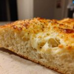 Cross-section view of a slice of Tasty Garlic Bread With Cheese showing melted, stretchy mozzarella and a golden, herb-topped crust.