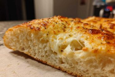 Cross-section view of a slice of Tasty Garlic Bread With Cheese showing melted, stretchy mozzarella and a golden, herb-topped crust.