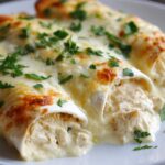 Close-up of two White Chicken Enchiladas with Creamy White Sauce, topped with melted, slightly browned cheese and fresh parsley.