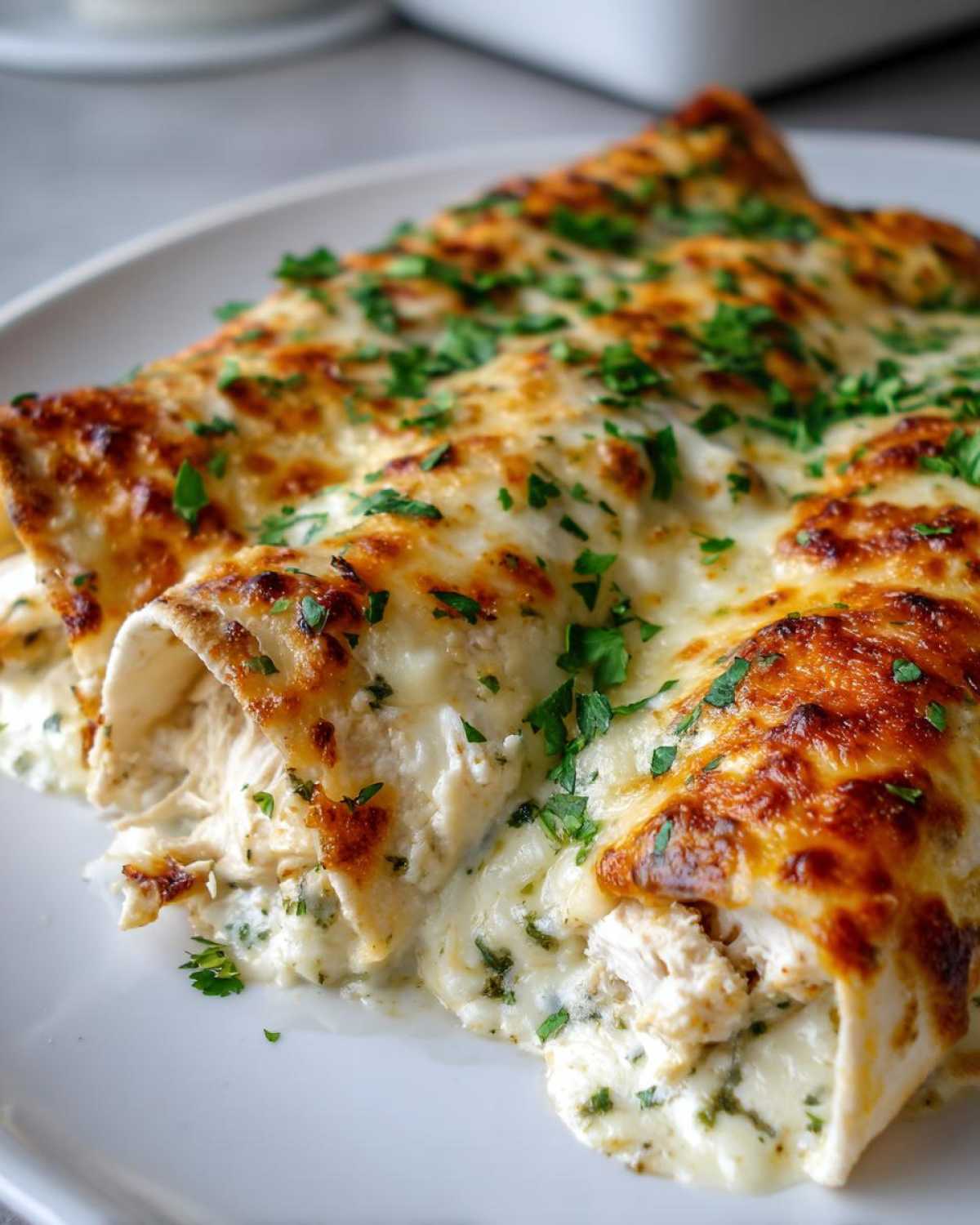Close-up of baked White Chicken Enchiladas covered in bubbly, melted cheese and fresh parsley.