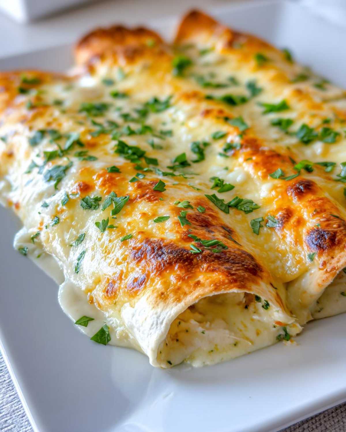 Close-up of baked White Chicken Enchiladas covered in melted, bubbly cheese and fresh parsley.